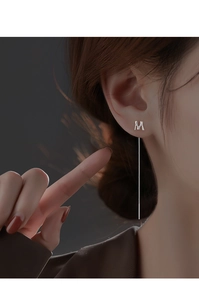 Close-up of silver letter M long tassel earring worn by a model in minimalist style