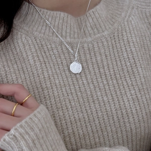 Close-up of 925 sterling silver wavy textured round pendant necklace on beige sweater
