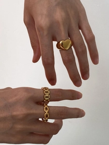 Close-up of gold chain style rings and a heart ring worn on a hand against white wall
