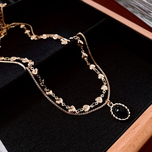 Detail of gold layered necklace with heart links and a black oval pendant on velvet