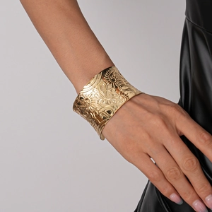 Close-up of wide gold cuff bracelet featuring embossed paisley and sunflower patterns