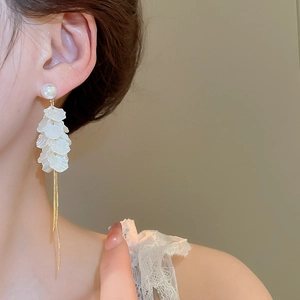Detail of long fringe earrings featuring white petals, pearls and gold tassel chains