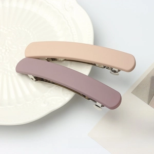 Macro view of matte minimalist hair clips in soft pink and purple on white ceramic plate