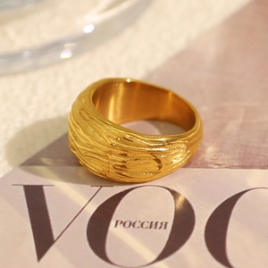 Anello largo dorato con trama ondulata irregolare su sfondo di una rivista di moda