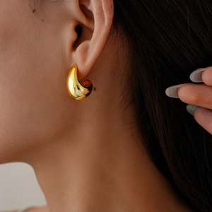 Close-up of model wearing polished gold water drop stud earrings with a geometric C-shape