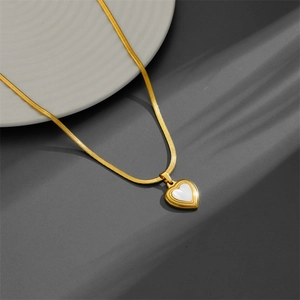 Collier chaîne serpent dorée avec pendentif cœur en nacre sur une assiette en céramique