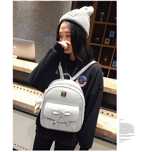 Detail of grey bow backpack with bear charm shown in a cozy cafe setting on a model