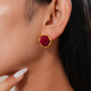 Close-up of a vintage round gold-rimmed earring with dark red velvet inlay on a model