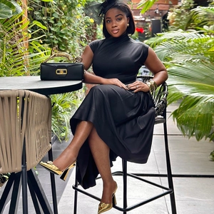 Detail of elegant black sleeveless dress with gold leopard handle handbag in garden setting