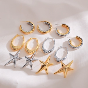 Minimalist gold and silver star earrings and textured hoops set on beige silk fabric