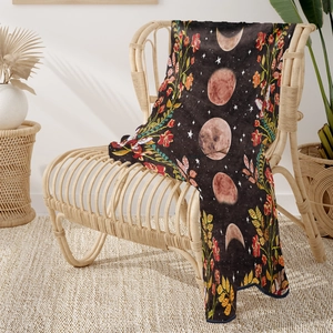 Bohemian moon phase flannel throw blanket with floral patterns on a rattan chair