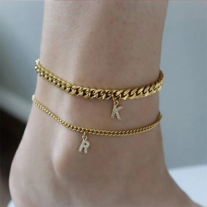 Gros plan sur une chevillère double couche dorée avec pendentifs lettres K et R sertis