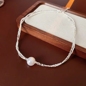 Gros plan d'un collier à double rangée de perles argentées avec une perle blanche nacrée