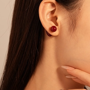 Gros plan de boucles d'oreilles cœur en résine bordeaux portées sur l'oreille