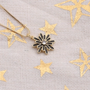 Macro shot of gold-plated daisy pendant with black enamel petals and zircon center
