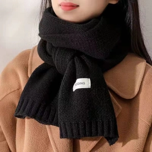 Detailed view of a soft black knitted scarf with a white label on a stylish brown coat