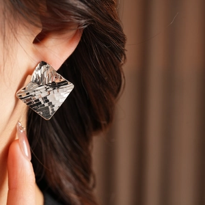 Close-up of diamond-patterned silver earrings on model with high-shine metallic finish