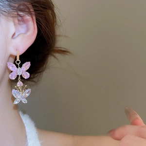 Close-up of model wearing gold butterfly pendant earrings with pink and clear crystals