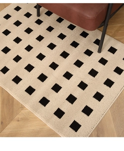 Detail of beige woven cotton-linen rug with black square pattern on light wood floor