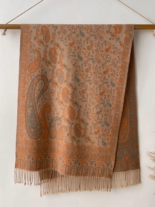 Detail of orange and grey paisley pattern scarf with fringes hanging on wood bar