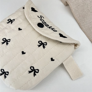 Dettaglio macro della pochette beige trapuntata con fiocchi neri e chiusura bottone
