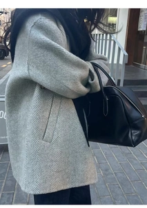 Detail of grey herringbone wool coat texture paired with a black leather handbag