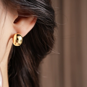 Close-up of a minimalist gold bean-shaped stud earring worn by a model on the left ear