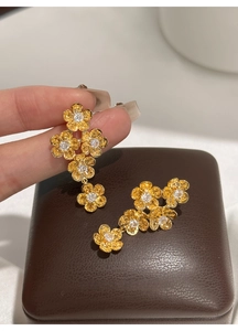 Detailed view of long gold floral earrings with matte petals and sparkling zircons