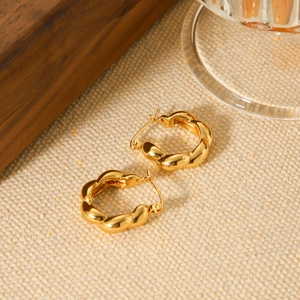 Pair of elegant 18K gold plated stainless steel twisted hoop earrings on fabric background
