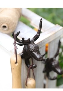 Close-up of vintage cast iron deer head wall hook holding a wooden garden tool