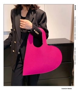 Detail showing high-saturation magenta felt heart handbag styled with a black blazer