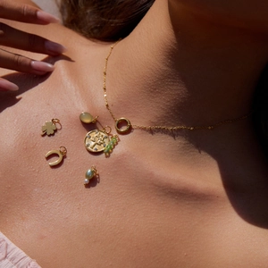 Collana in acciaio dorato con ciondoli a perla e quadrifoglio alla luce del sole
