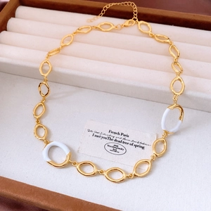 Close-up of gold oval link necklace with white enamel accents on a jewelry display tray