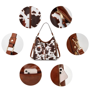 Detail view of brown and cow print tote bag with multiple zippers and tassel hardware