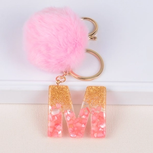Detail of pink pompom keychain with resin letter M featuring gold glitter and shell flakes