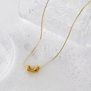 Minimalist gold U-shaped pendant necklace displayed on white foam with glass backdrop