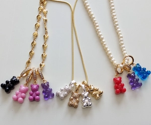 Detail of colorful gummy bear pendants on gold heart, snake, and pearl necklaces