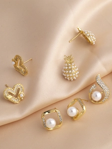 Detailed view of pearl and rhinestone earrings with heart and pineapple shapes on silk