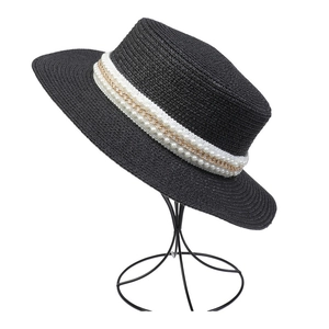 Detailed close-up of a black straw hat with white pearl trim and gold chain on a stand