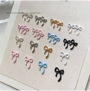 Close-up of assorted alloy bow nail charms in metallic and matte finishes on a display card