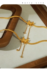 Macro detail of gold-plated titanium anklet with butterfly charms and tassel chains