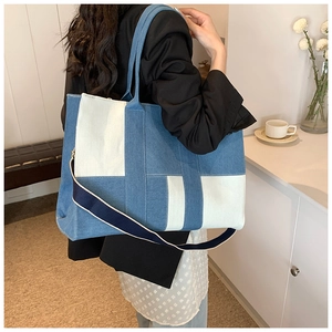 Detail view of large denim patchwork tote bag with striped shoulder strap and woven handles
