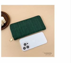 Detail view of dark green striped long wallet with zip and size reference next to a phone