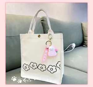 Detail of pink cat charm and floral pattern on a white canvas tote bag over a gray sofa