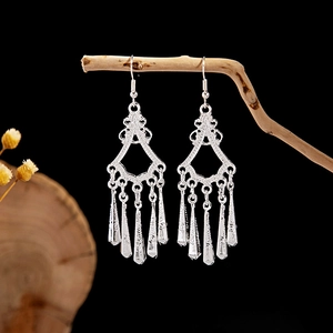 Macro shot of ethnic silver hollow leaf tassel earrings hanging on a rustic wooden branch