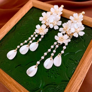 Detail of floral tassel earrings with white shell petals and golden chain fringe accents