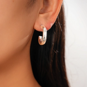 Detail view of a minimalist silver-finish C-shaped metal hoop earring worn by a model