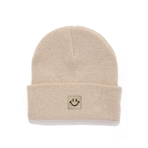 Detail shot of a beige knitted kids beanie featuring a brown square smiley face patch