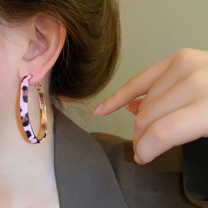 Close-up of model wearing large pink and black leopard print hoop earrings with gold trim