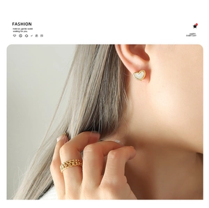 Detail of heart shell stud earring with gold border and chain-style gold ring on model